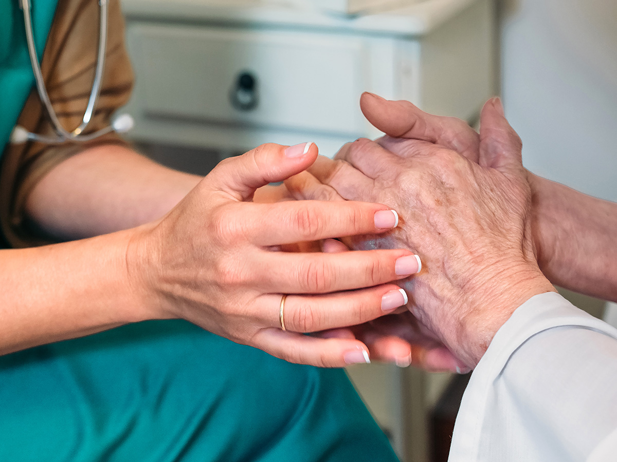 Female nurse holds the hands of an elderly patient