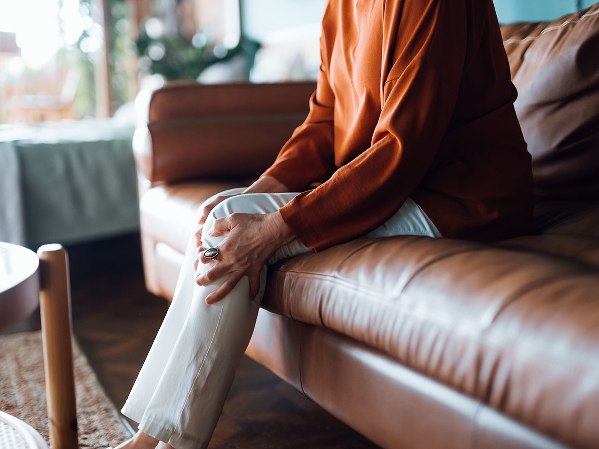 Cropped shot of a senior woman holding leg while sitting on sofa in the living room