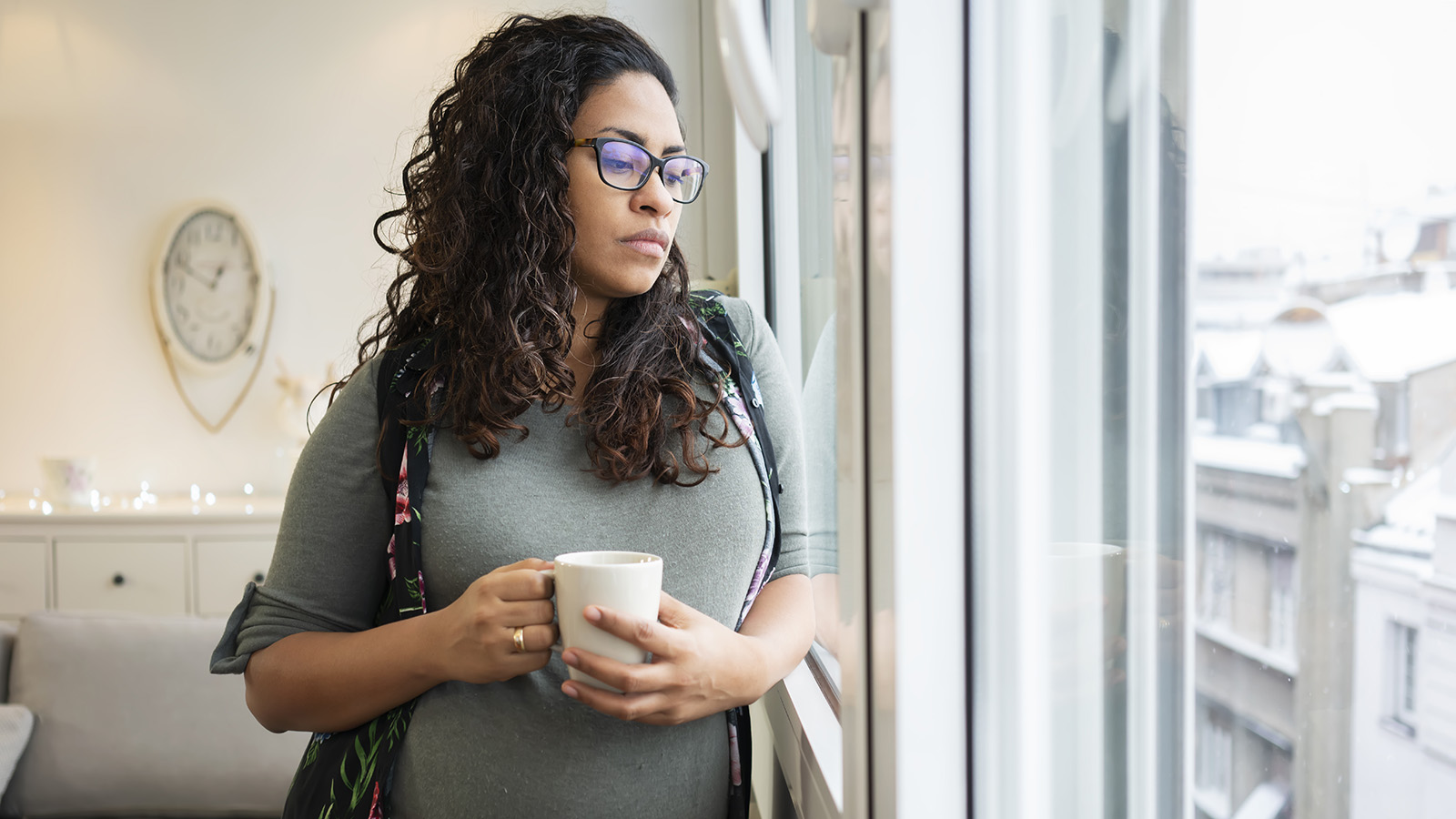 Pregnant woman holding coffee by the window