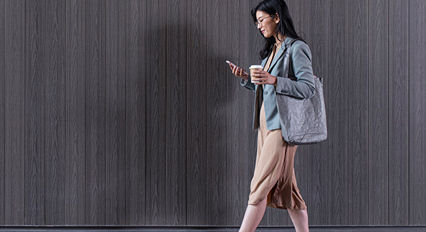 Adult woman with large bag walks while looking at her phone