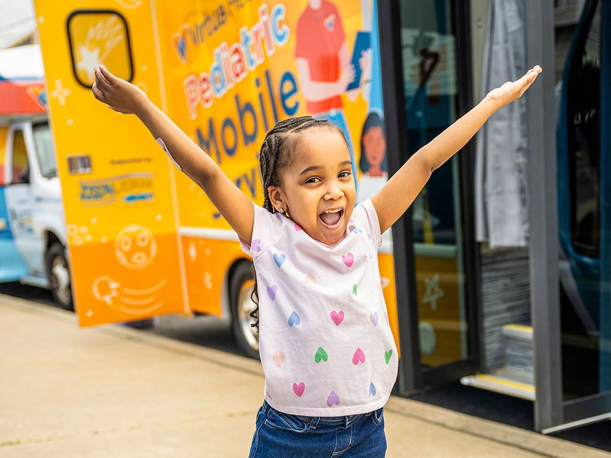 little girl with arms outstretched in front of a mobile health screening van