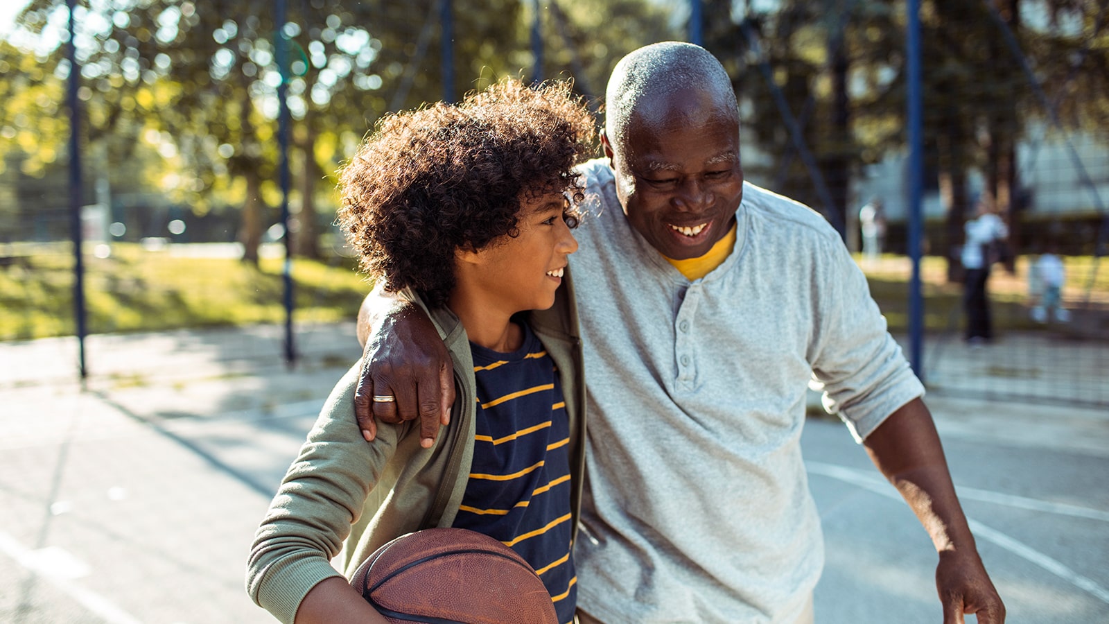 A grandfather and his grandson embrace outside while playing basketball