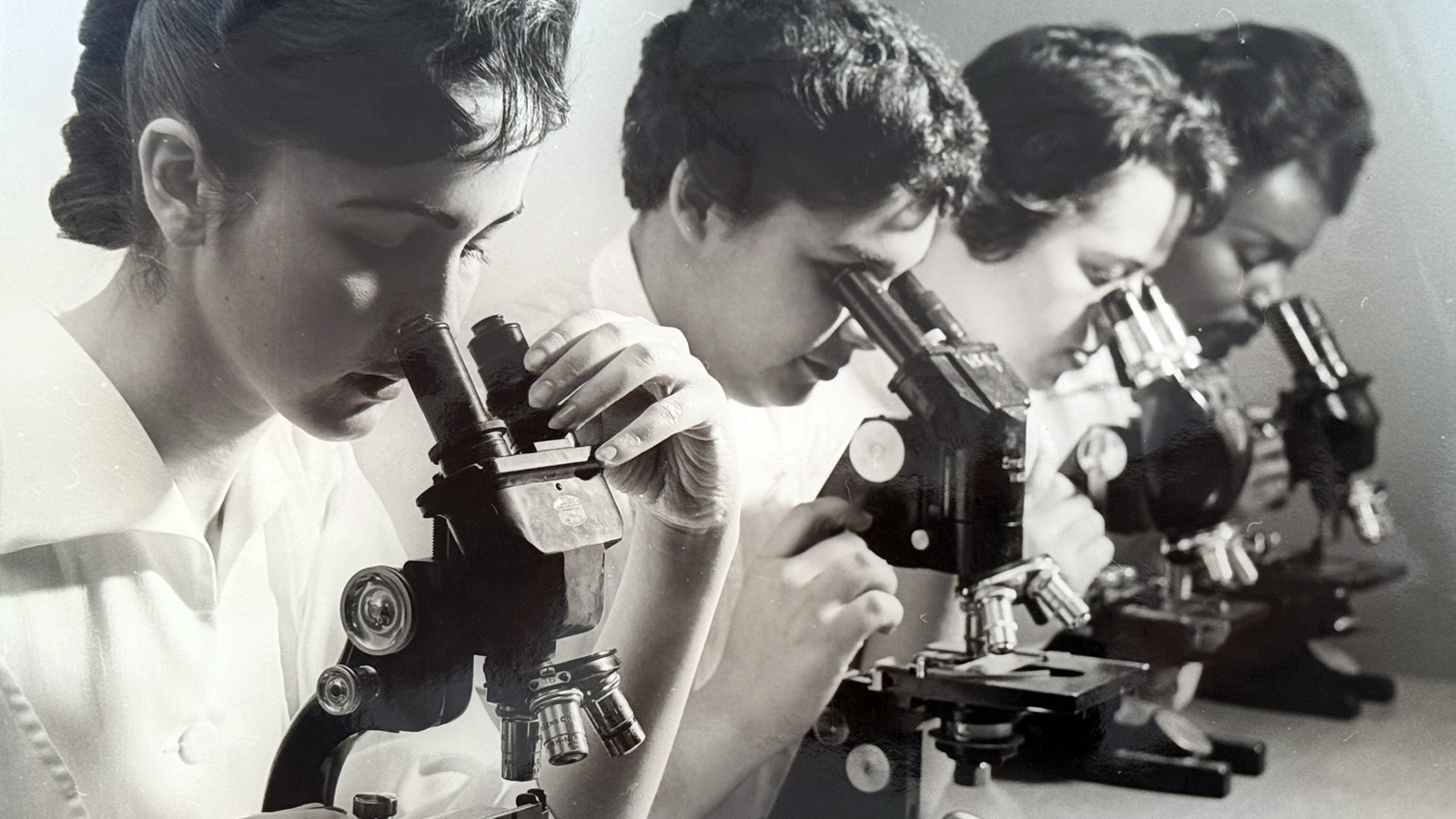 Women in a nursing school circa 1950s look under microscopes