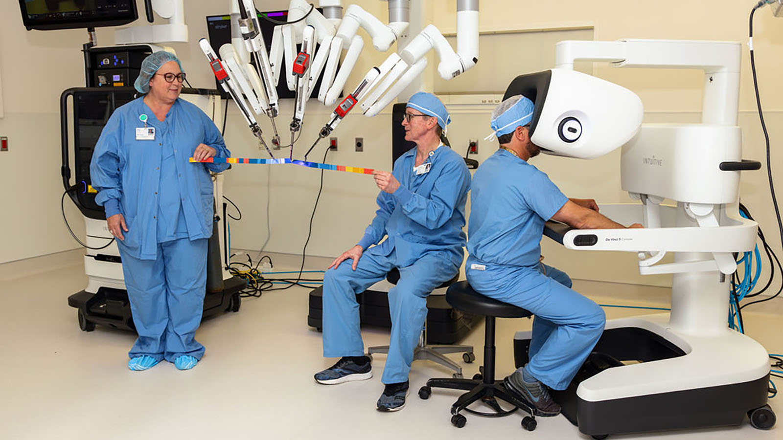 Two male and one female medical staff members in blue scrubs work on medical machinery