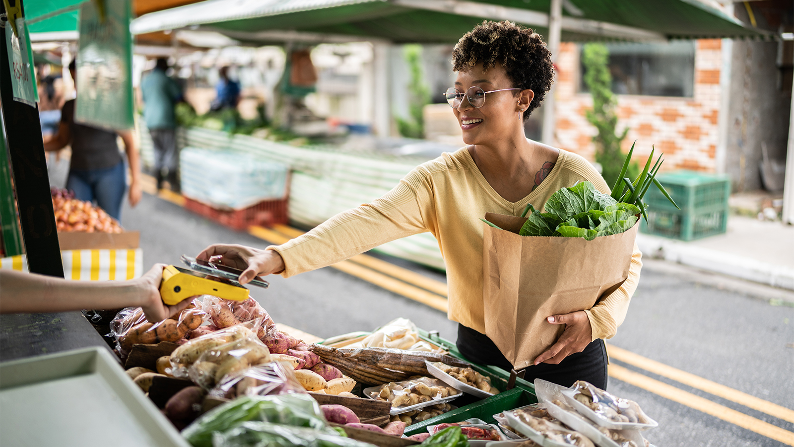 A woman in her 40s looking using her cell phone to pay for healthy vegetables at a market