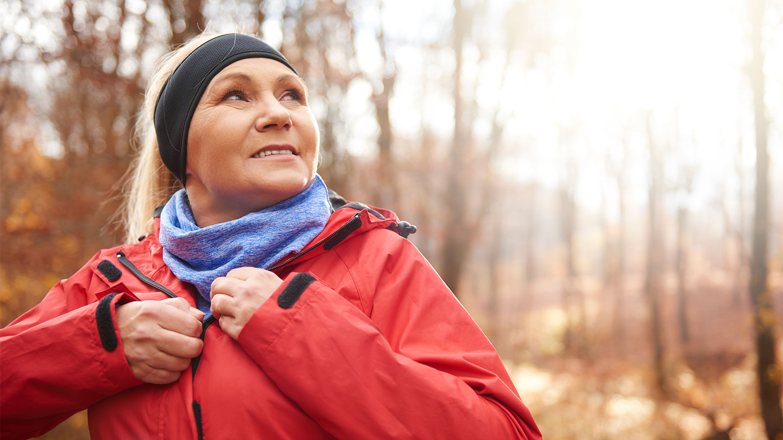 Middle-aged woman with headband and scarf on walking outside in late fall, unzipping her coat