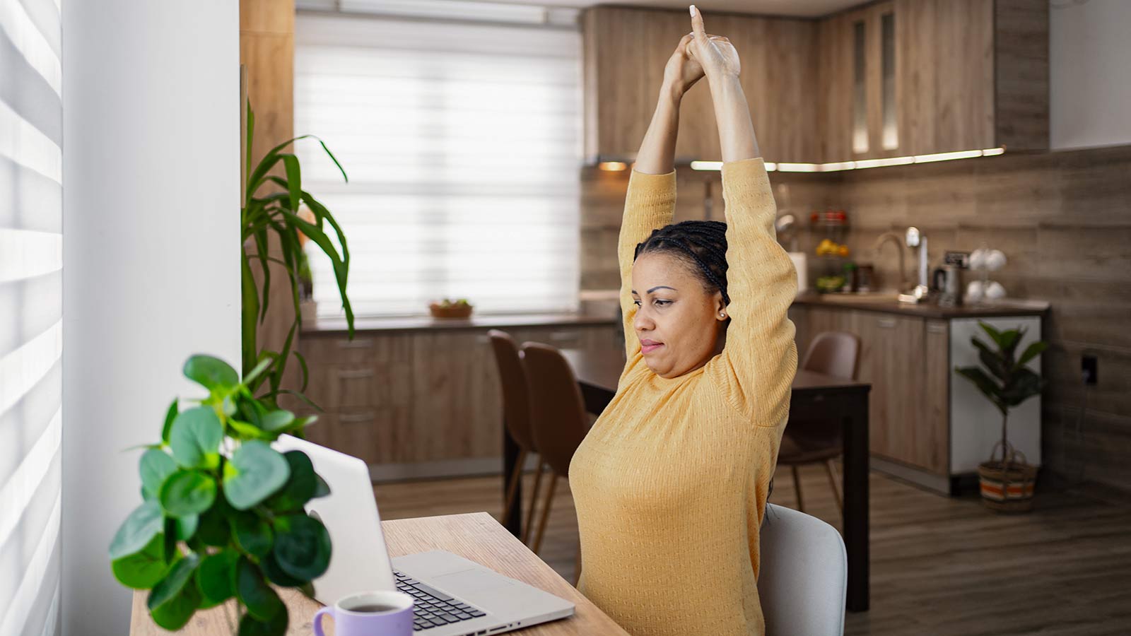 woman sitting at her desk and stretching while working on a laptop