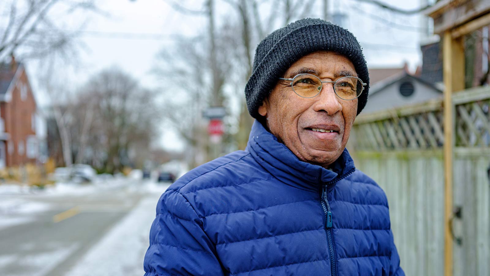 man taking a walk through the neighborhood wearing a winter coat and hat
