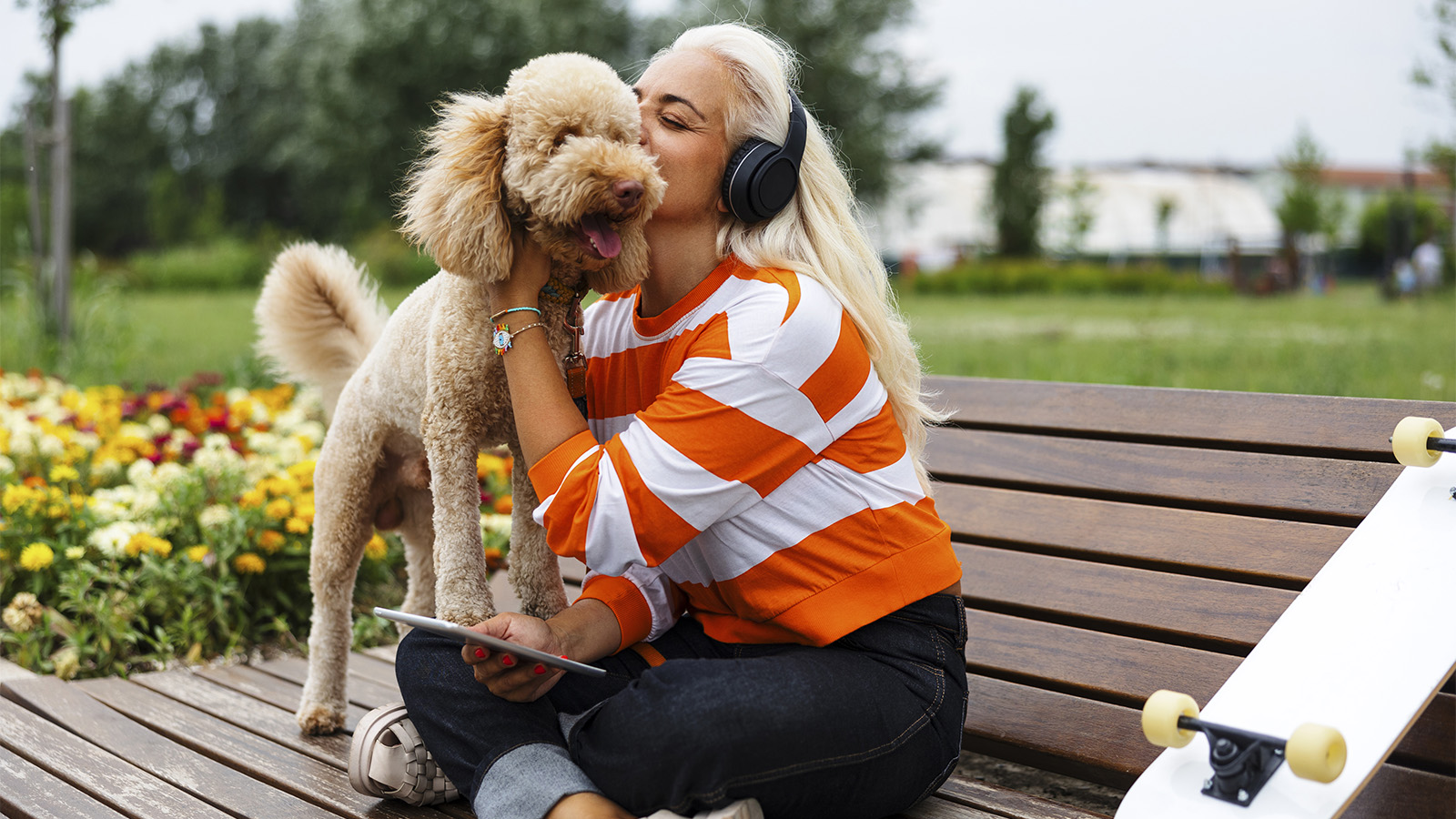 Woman petting and kissing her dog on a bench in a public garden