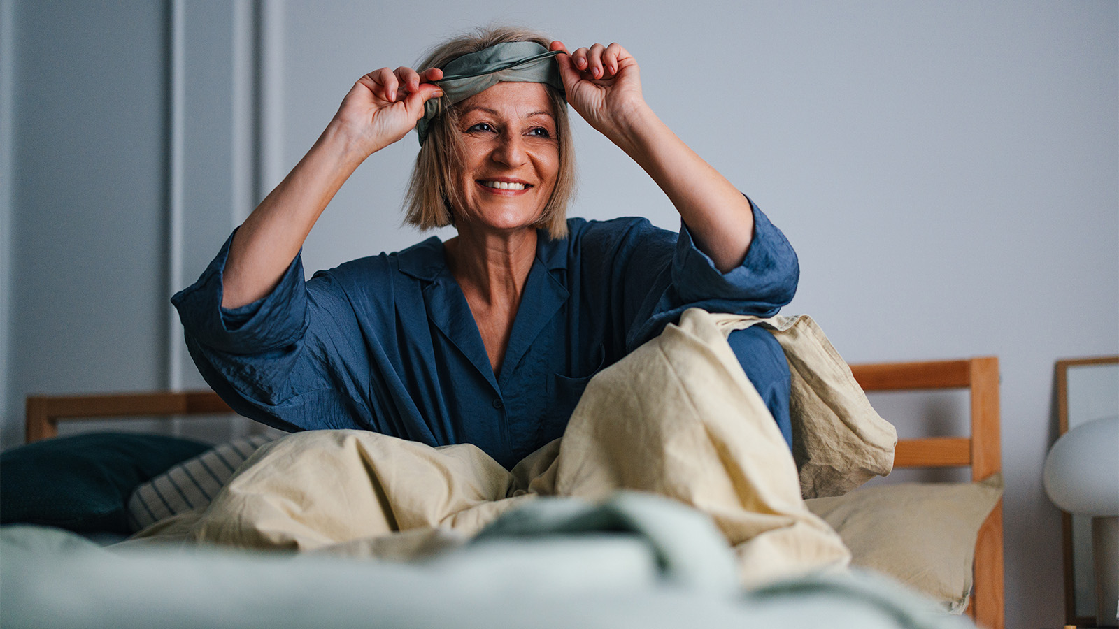 Middle-aged woman waking up, smiling, and removing a sleep mask