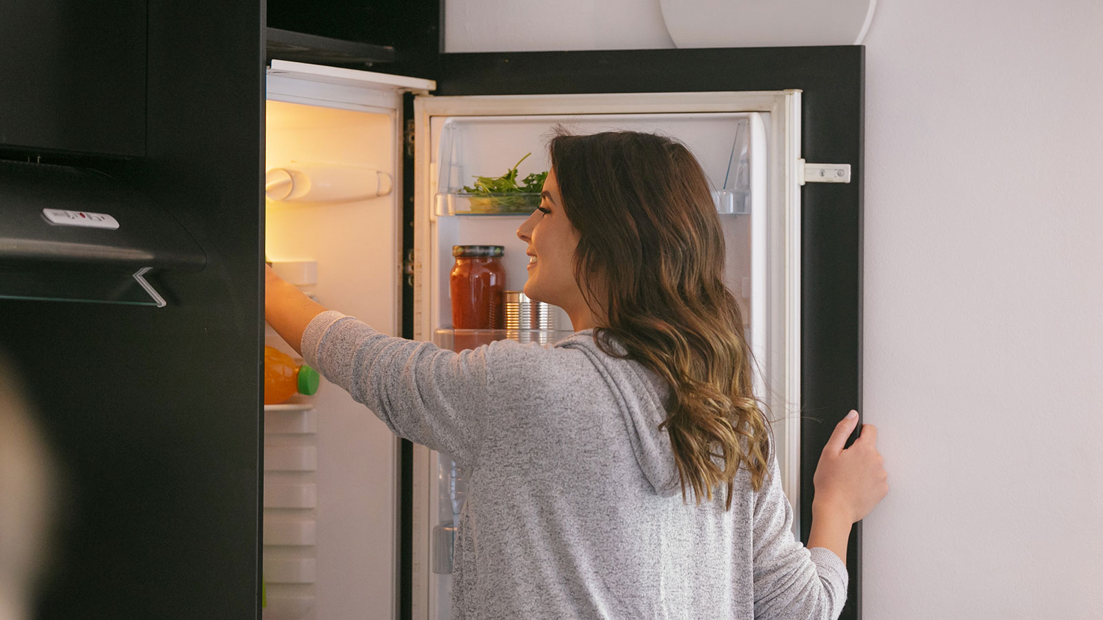 Woman standing at open refrigerator, grabbing an item from inside
