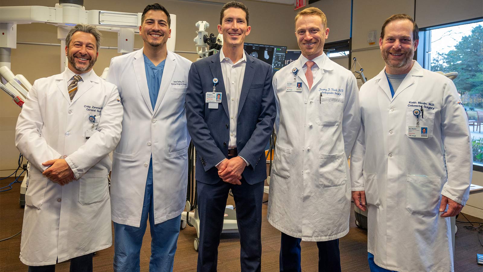 group of five Virtua Health doctor's in lab coats standing in front of robotic surgical equipment