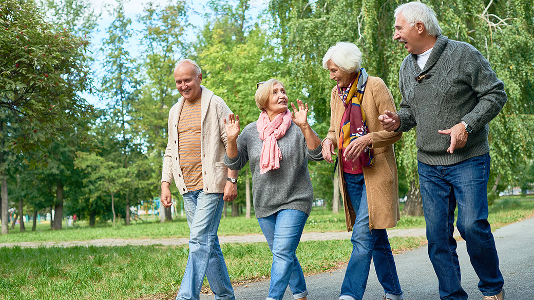 Two male and two female senior citizens walk on a tree-lined, paved path
