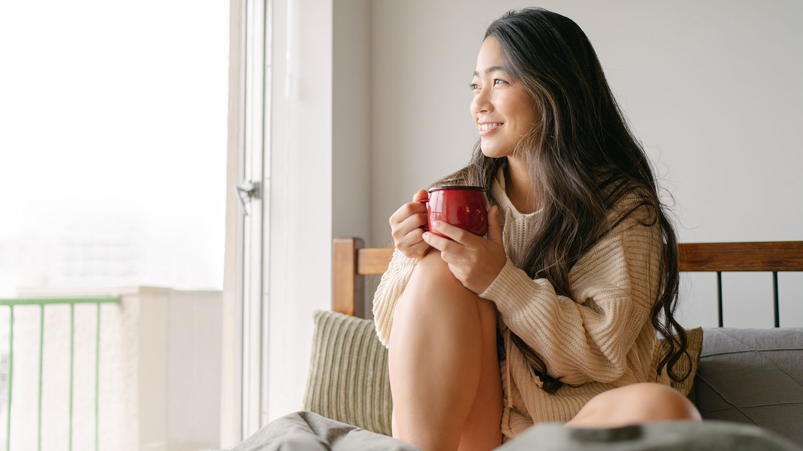 Young woman enjoying a cup of coffee and looking out the window in the morning