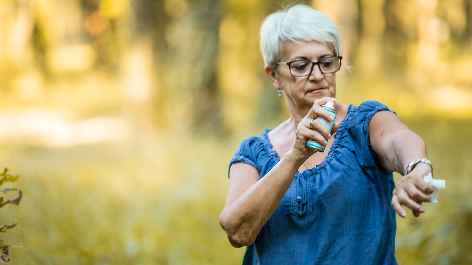 senior woman in natural setting spraying a can of bug repellent on her arm