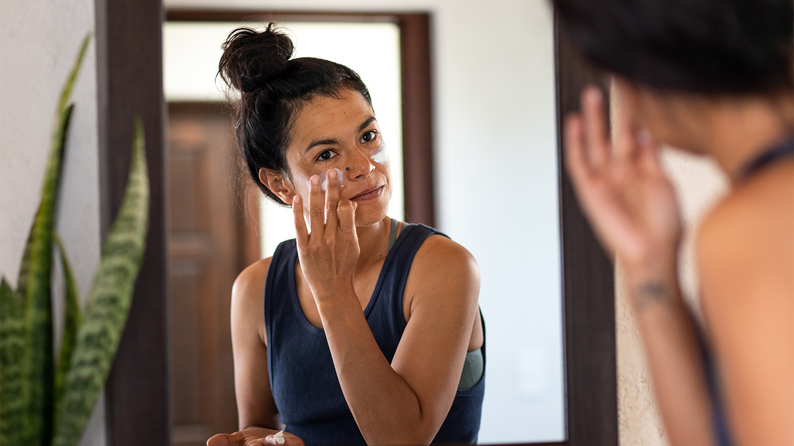 woman looking in mirror while applying sunscreen to her face