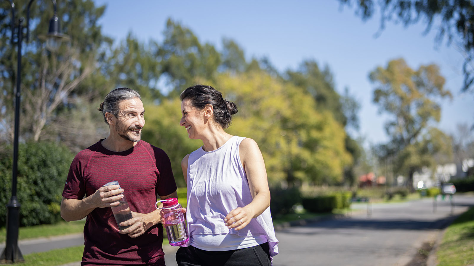 man and woman talking happily and holding water bottles in outdoor setting
