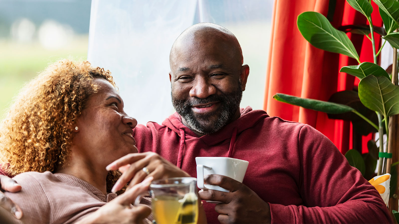Middle aged man and woman relaxing in front of a window in their living room, drinking tea and coffee