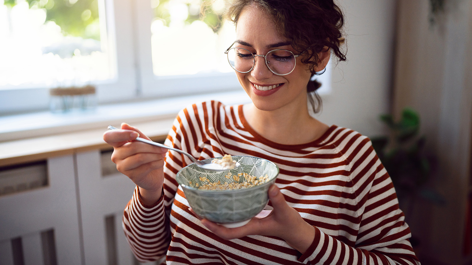 Young woman with glasses, smiling and eating a bowl of oats