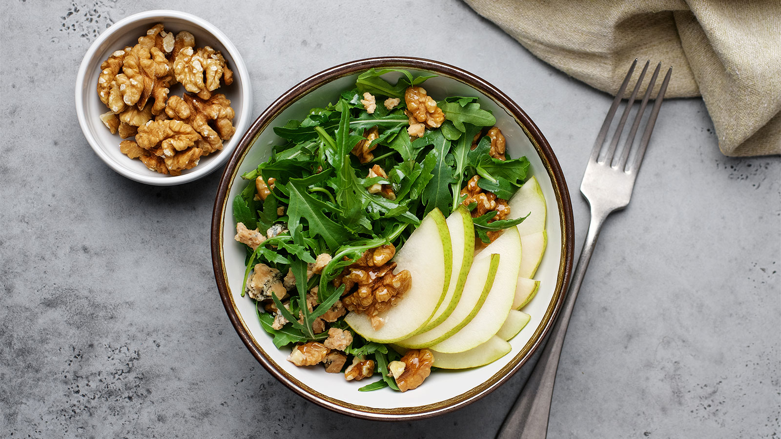 a salad with pears and walnuts with a bowl of walnuts next to it