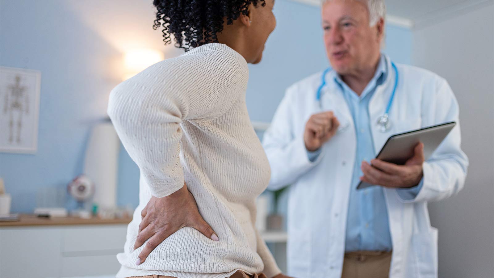 woman holding her lower back in pain while discussing with her doctor