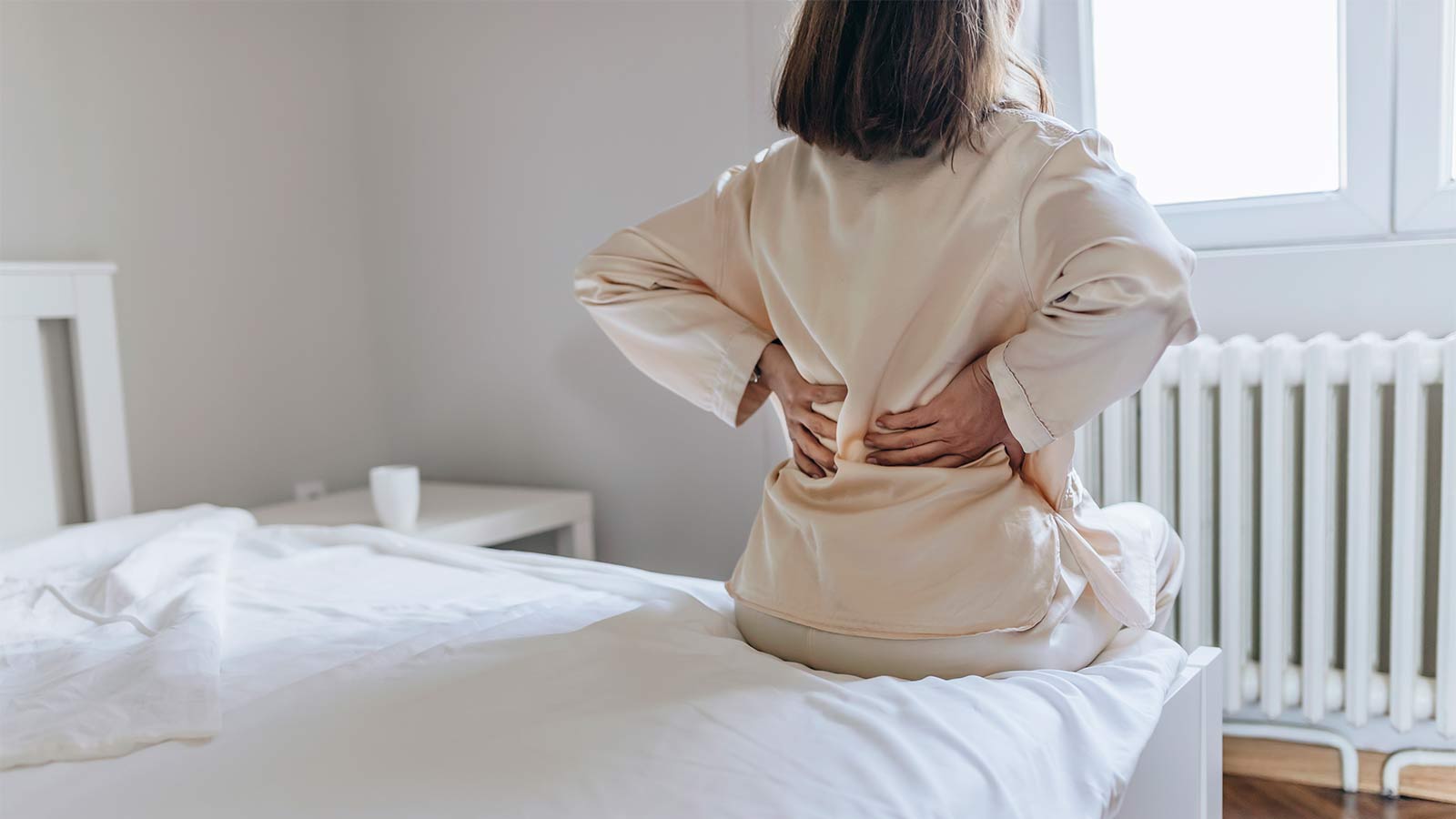 woman holding her lower back while getting out of bed