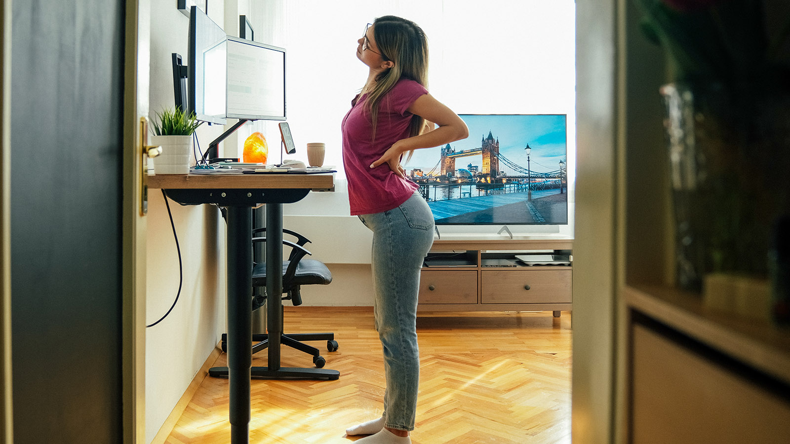 woman at a standing desk stretching her back