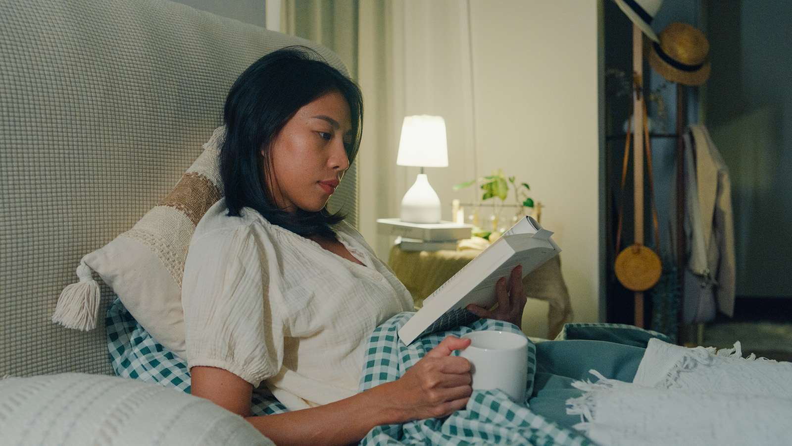 woman sitting up in bed reading a hardcover book