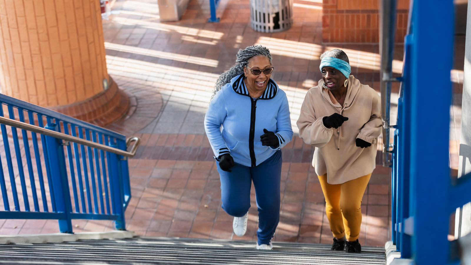Two female senior citizens wearing athletic clothing and jogging up a set of outdoor stairs