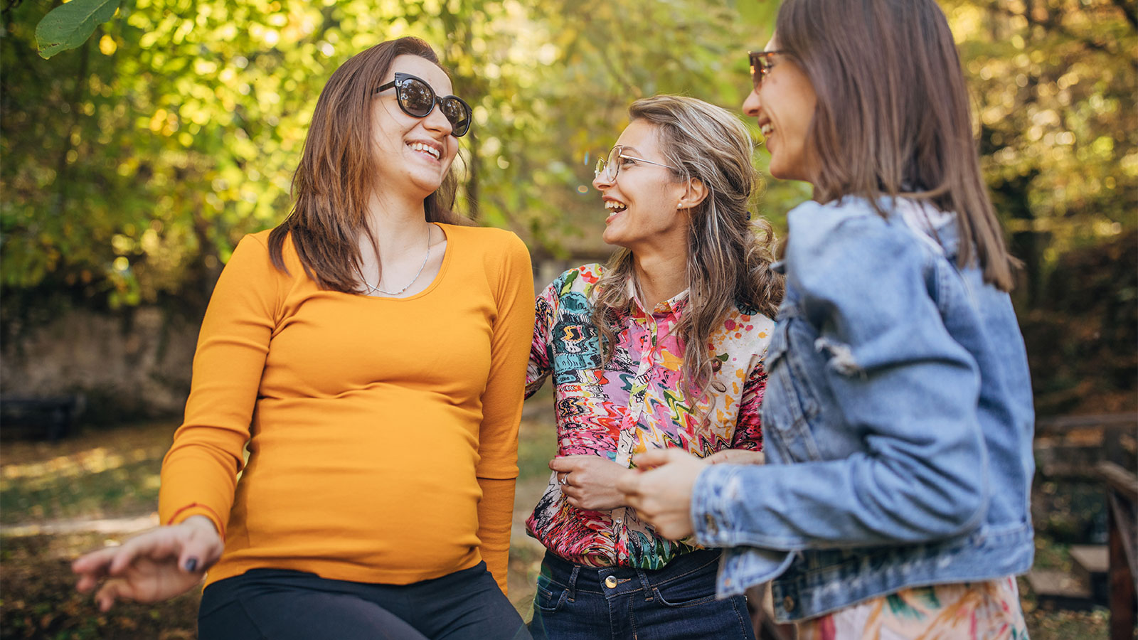 a pregnant woman laughing in an outdoor setting with two other women