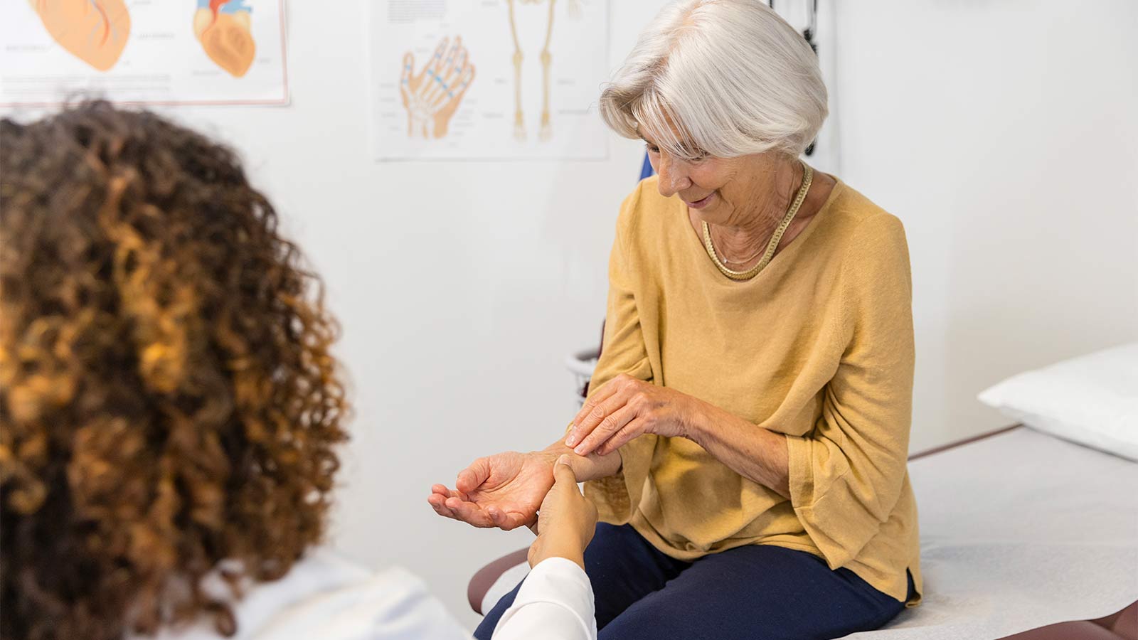 older woman sitting on an exam table discussing wrist pain with her doctor