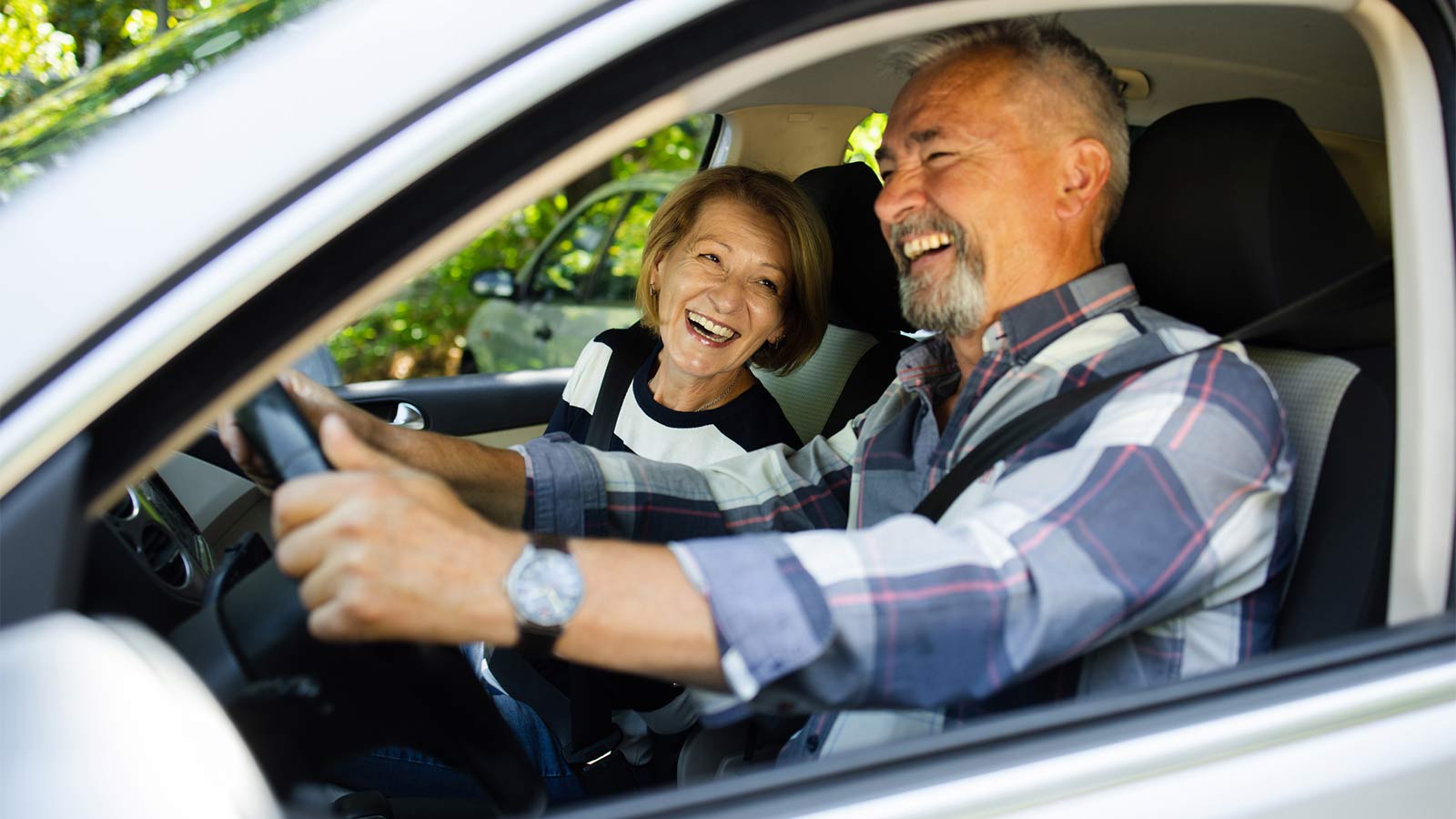 man smiling and laughing while driving a car with his wife in the passenger seat