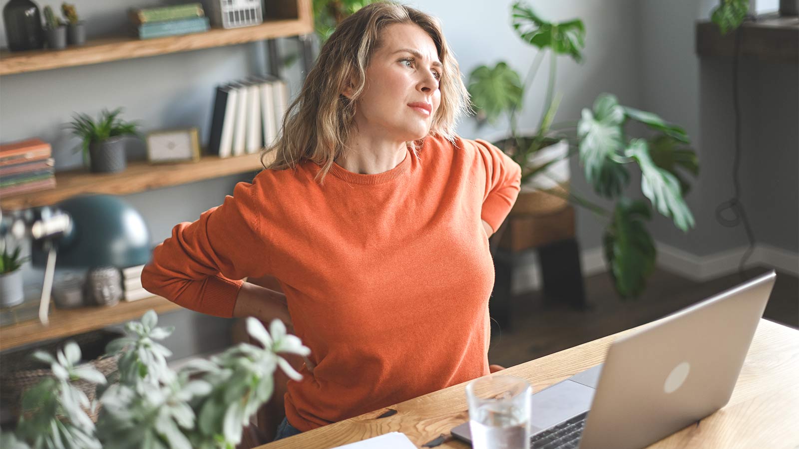 woman stretching her back while working from home on her laptop