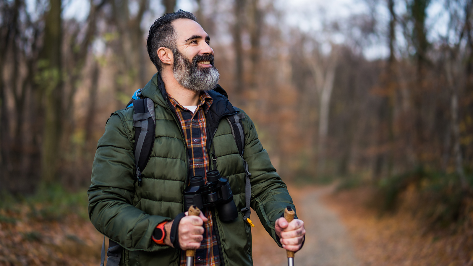 Man walking on path in woods with walking sticks