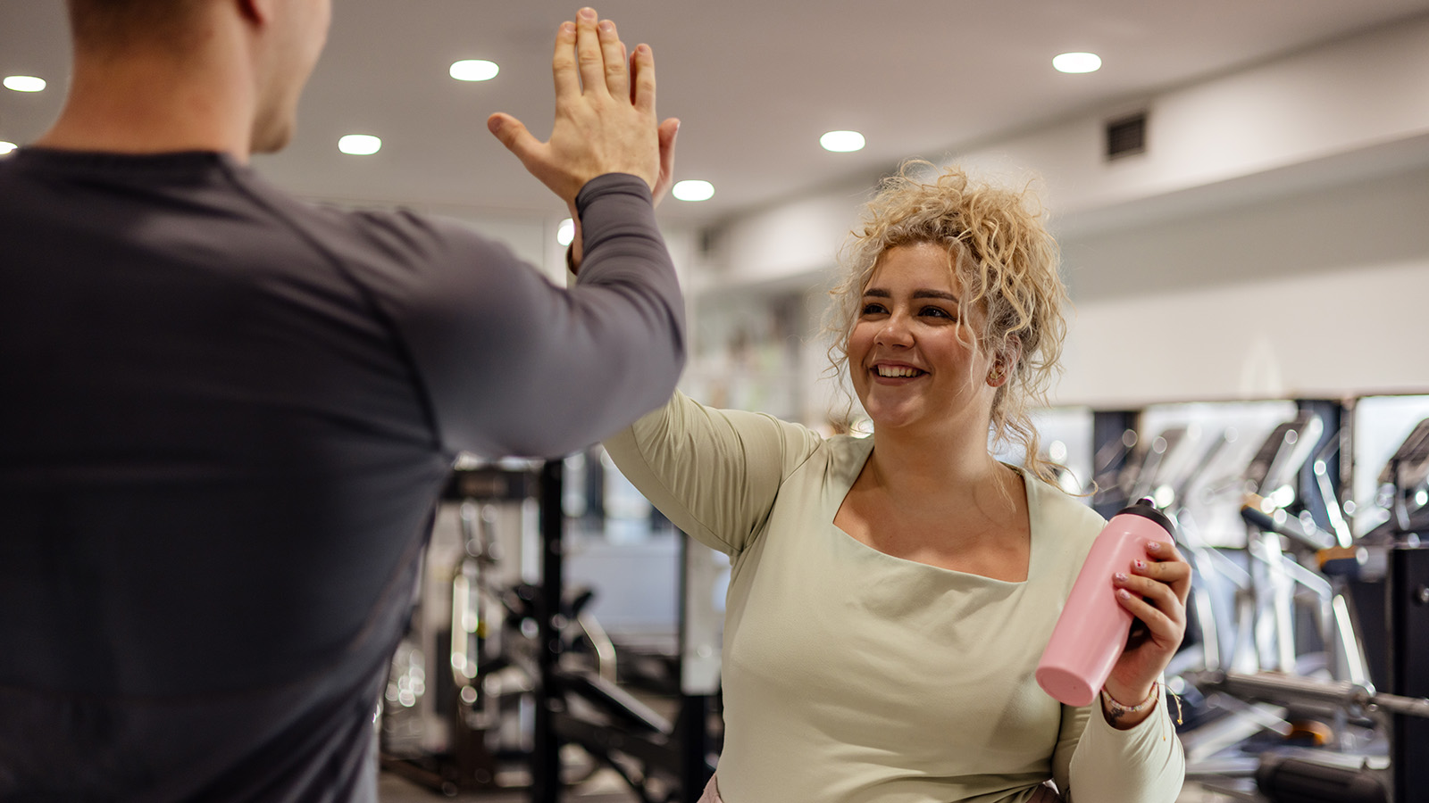 Woman holding pink water bottle smiling and high fiving a male at a gym