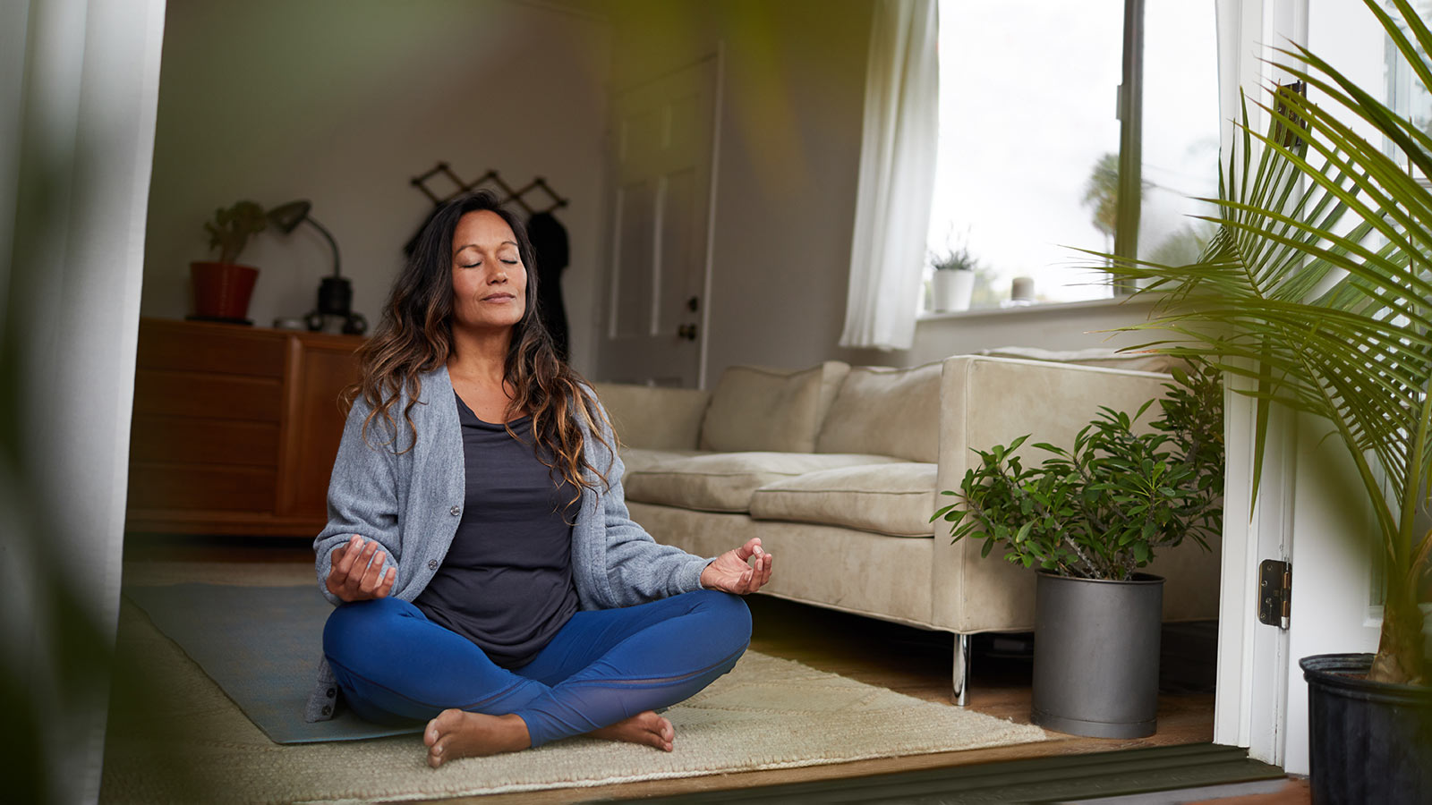 woman sitting cross-legged on yoga mat with her eyes closed and her hands on her knees with index fingers and thumbs forming a circle