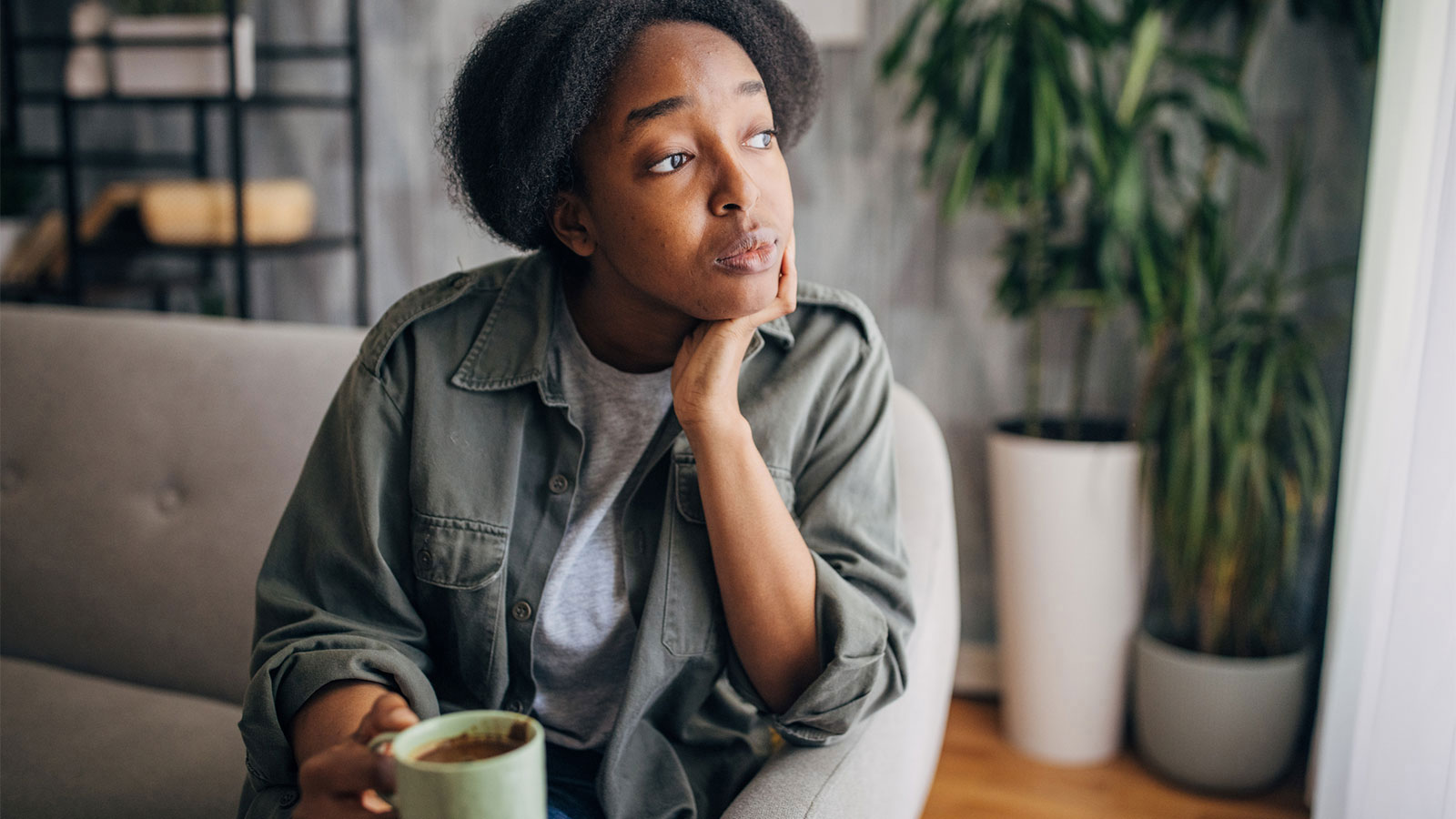 young woman drinking a cup of tea and looking out the window