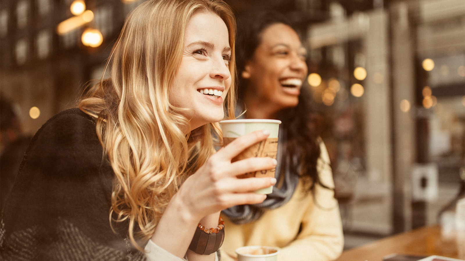 Two women smiling at a coffee shop, one is holding a cup of coffee