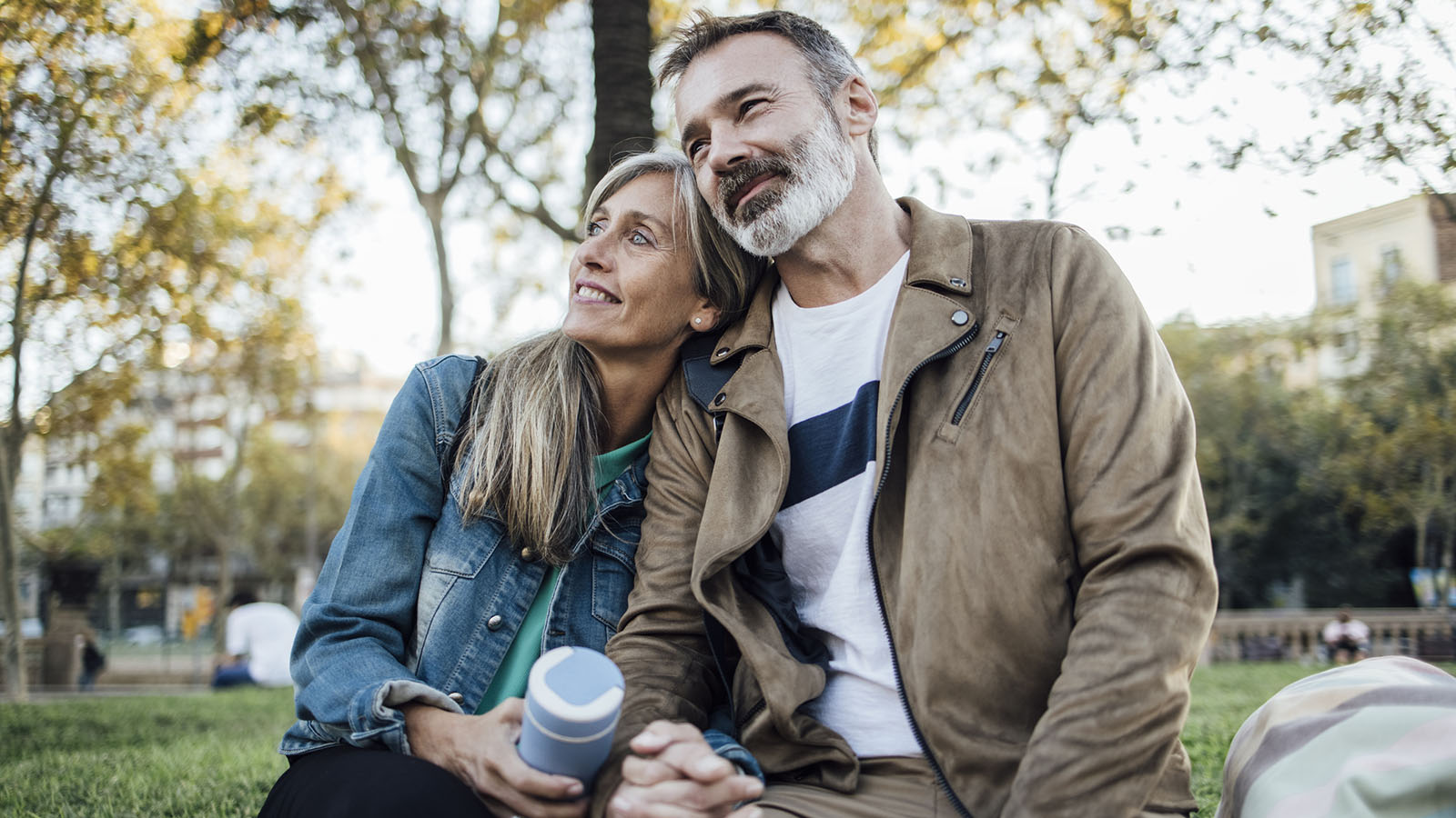 middle-aged couple smiling and holding hands while sitting outside under trees