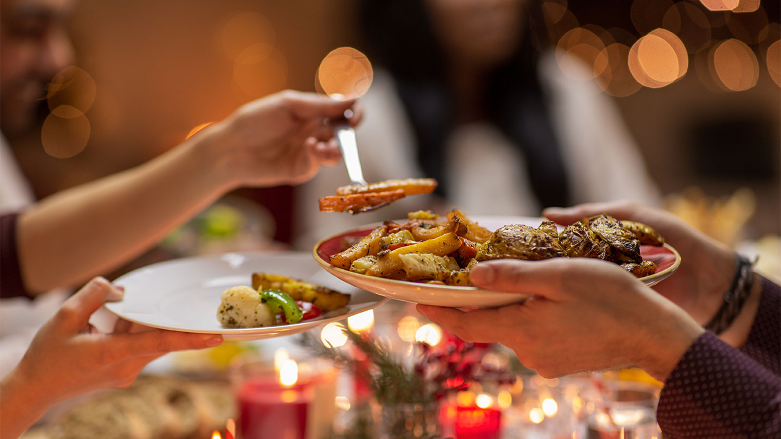 Hand of one person dishing out food to another in a festive, holiday atmosphere