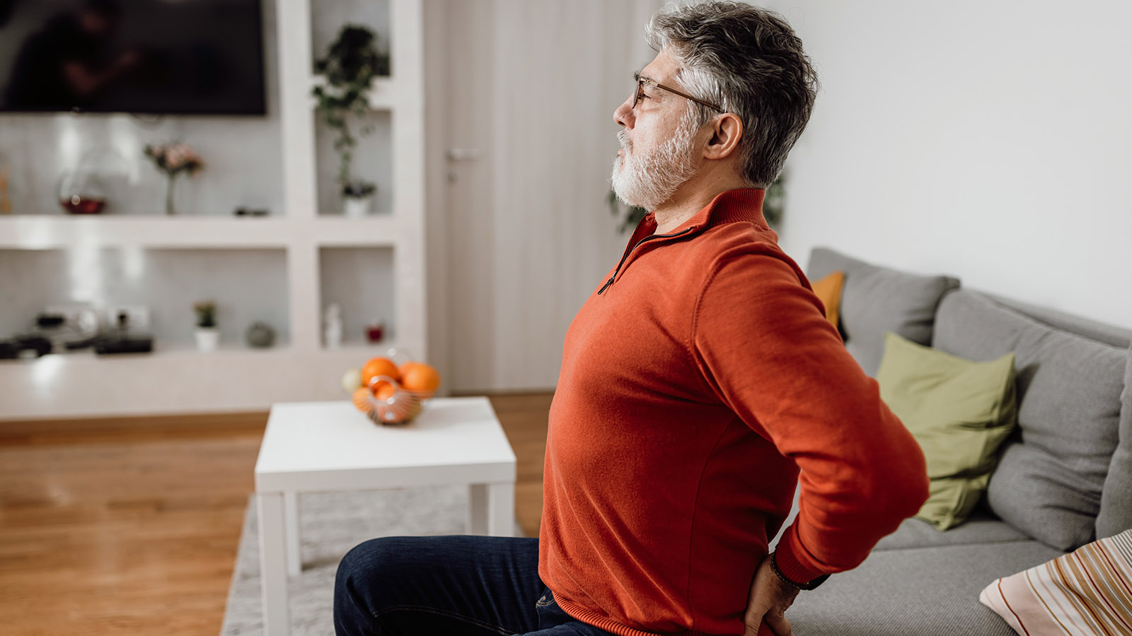 middle aged man sitting on the couch stretching his back