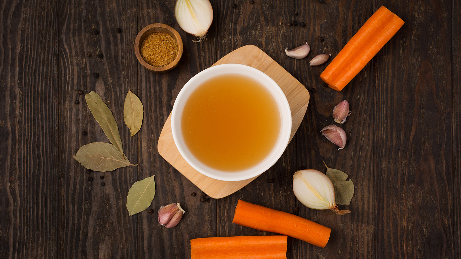 A bowl of broth with carrots and herbs arranged on a table