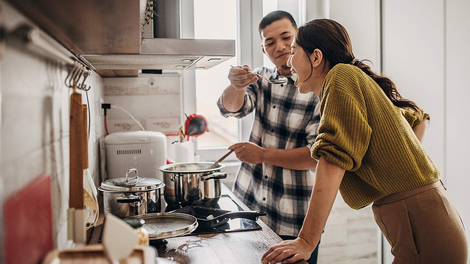 young couple tasting a sauce while cooking a meal together