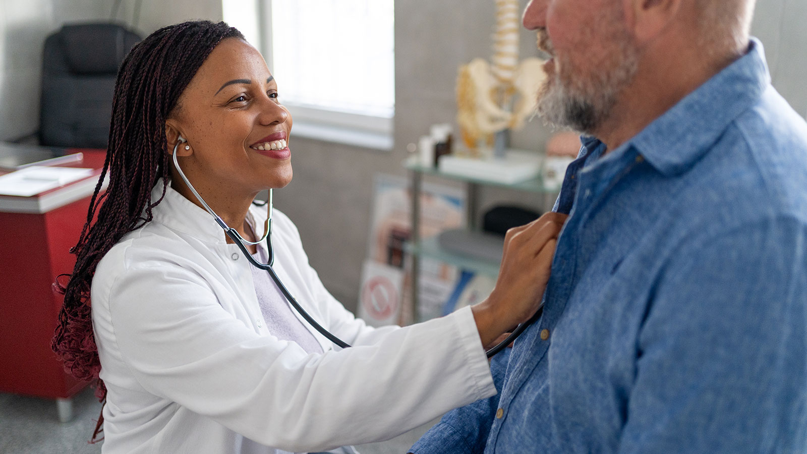 female doctor with stethoscope listening to male senior patient’s heartbeat in exam room
