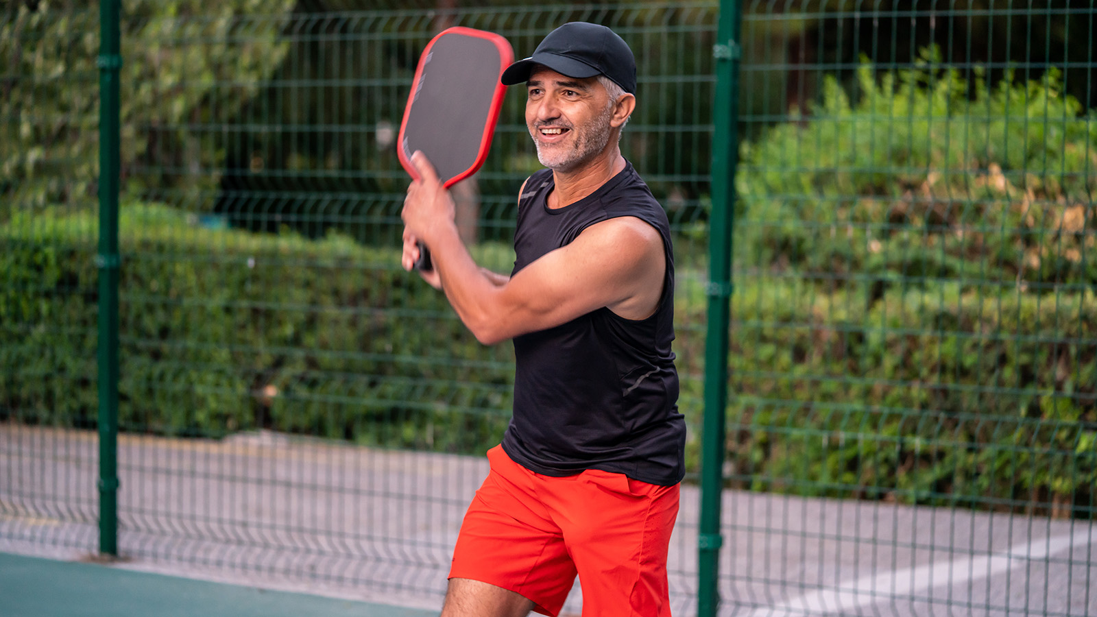 Middle-aged man playing tennis and smiling after swinging his racket