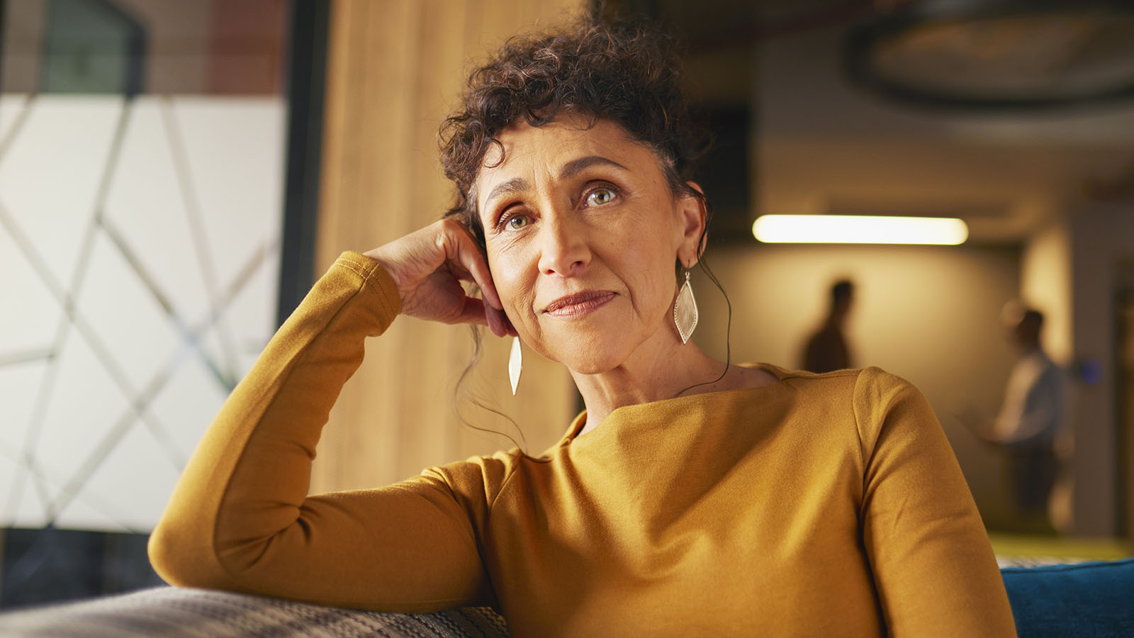 Older woman sitting on couch with two men in the background of the image