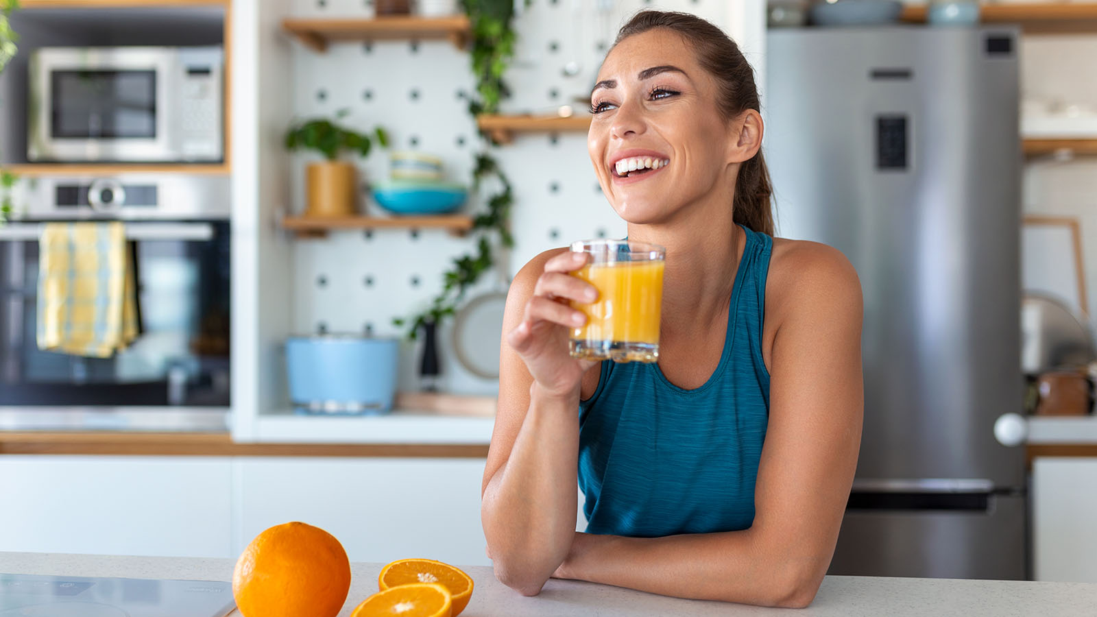 Woman holding glass of orange juice smiles in kitchen