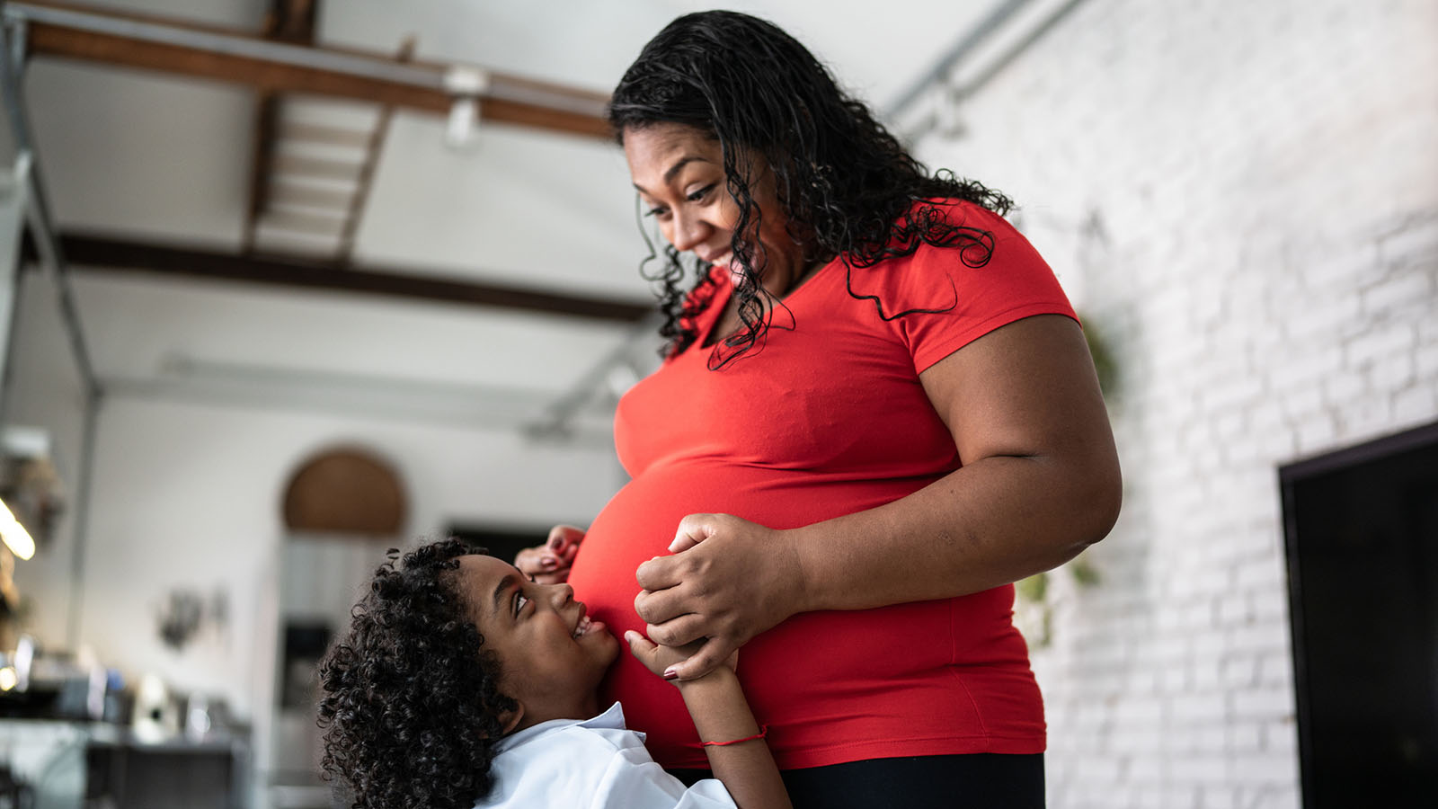 Pregnant woman who is overweight, smiling while young child hugs her belly.