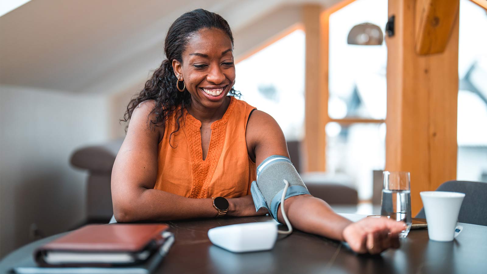 woman using a blood pressure cuff to measure her blood pressure at her kitchen table