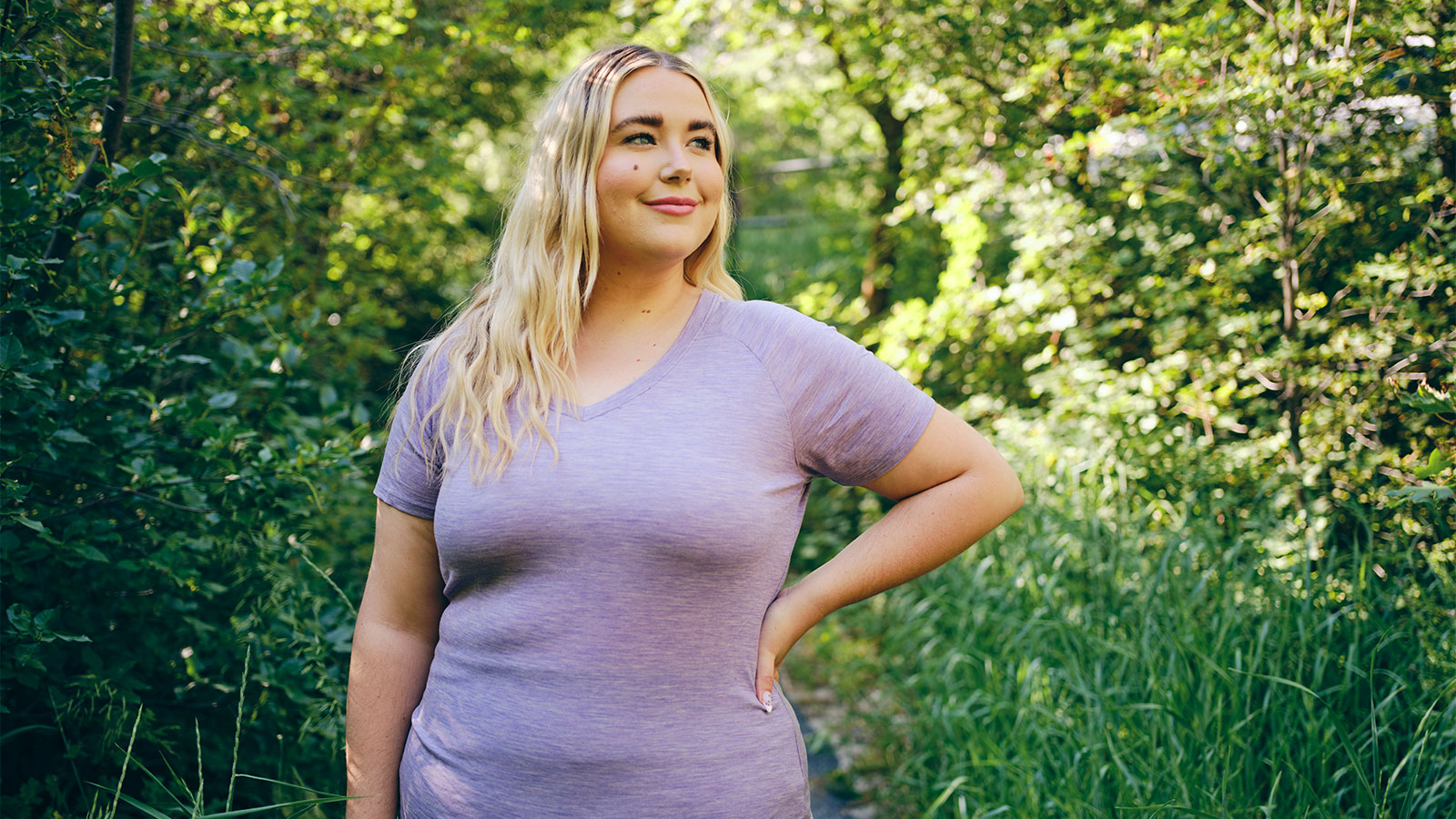Overweight young woman, standing in front of trees, with her hand on her hip